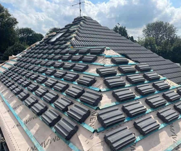 This is a photo of a new hip roof being installed. New felt, battens, and grey tiles have been installed, also a new velux window. Works carried out by FCB Roofing Cranfield