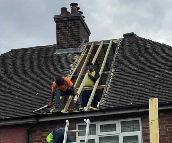 This is a photo of a roof repair being carried out. A section of the roof has been stripped and two roofers are replacing the rafters. Works being carried out by FCB Roofing Cranfield